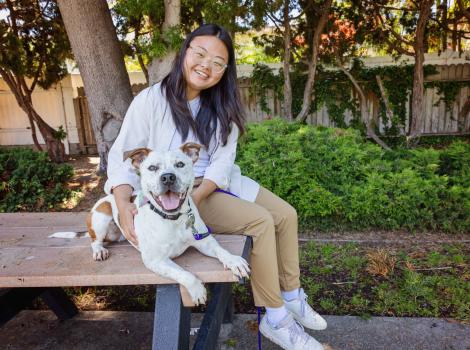 Shannon sitting on an outdoor table next to Felix the dog, both of them smiling