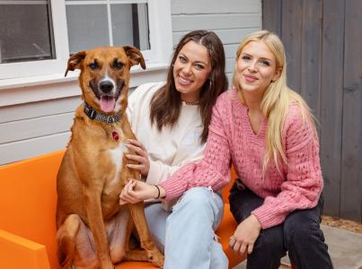 Two smiling people sitting on an outdoor couch with a dog