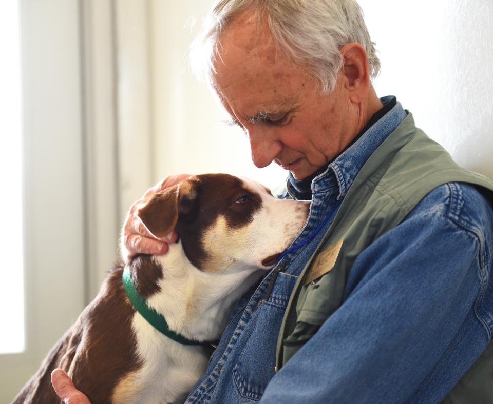 Person looking happily at a dog resting their head on their shoulder