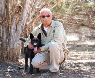 Person kneeling down next to a dog under a tree in the desert