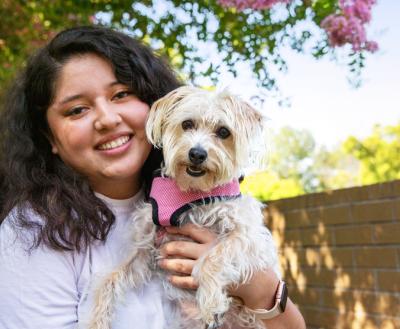 Smiling person holding a small white dog outside