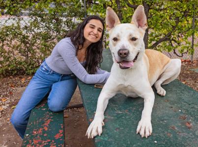 Smiling person sitting behind a large white and tan dog whose tongue is slightly out