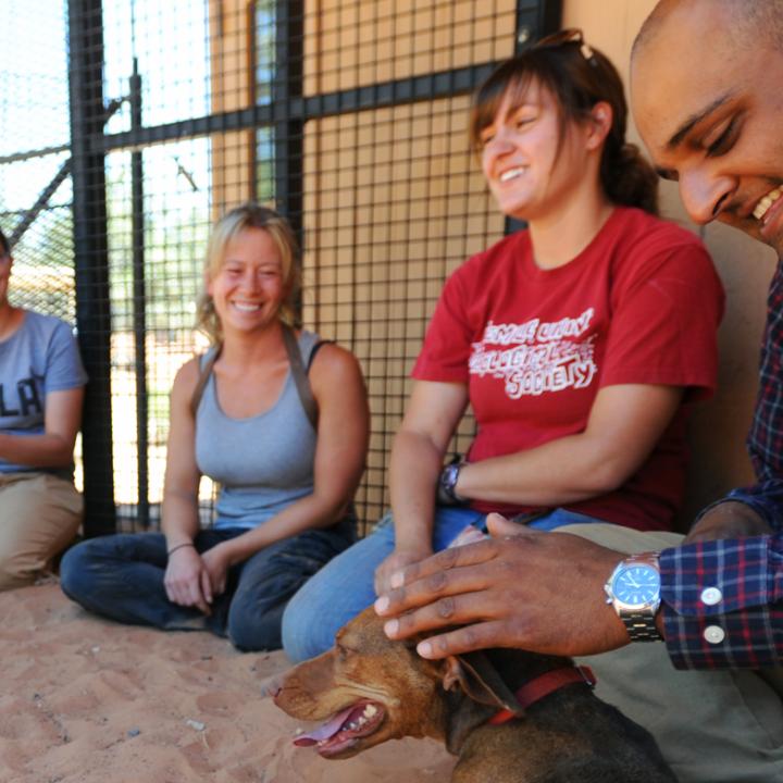 Group of smiling people sitting with a dog in sandy area in Utah desert