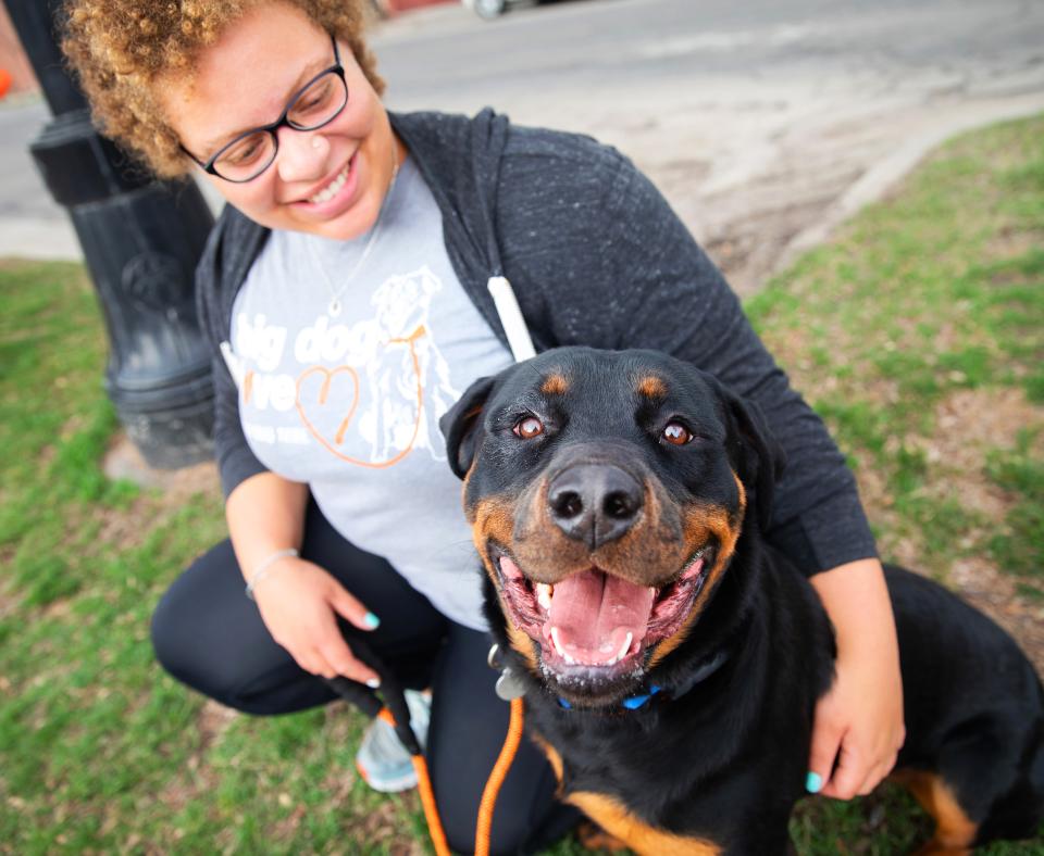 Smiling person kneeling next to a happy dog on the grass