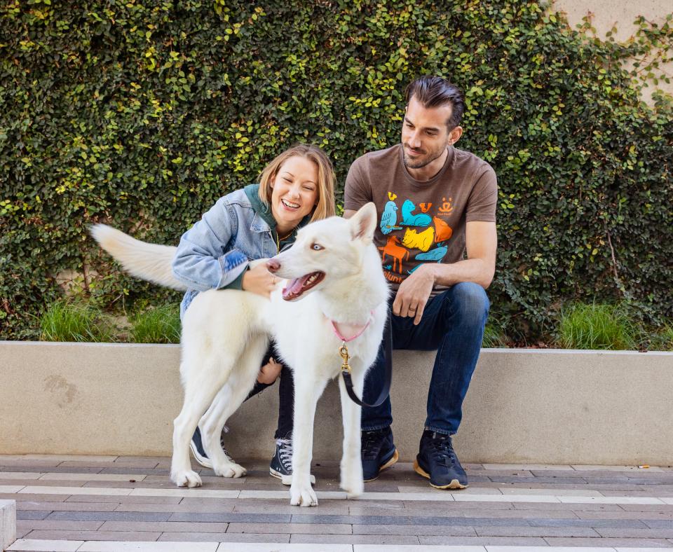 Two smiling people sitting with a dog outside