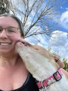 Mama the dog kissing the face of Ashley, who is smiing