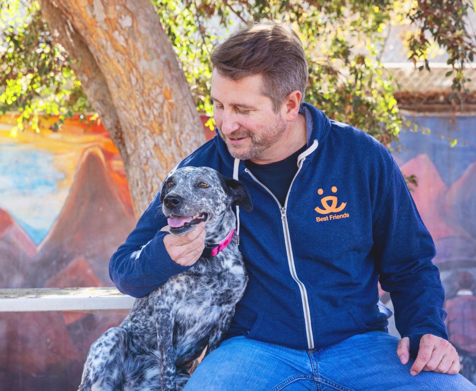 Smiling person wearing a Best Friends sweatshirt sitting with a dog outside