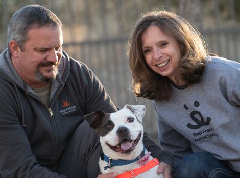 Bella the dog, smiling, between the two people who adopted her