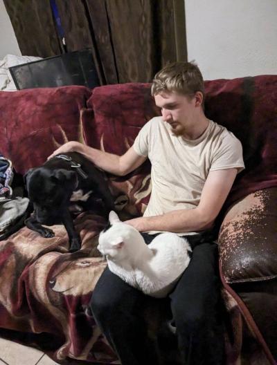 Jack the dog on a couch being pet by a person who has a cat on his lap