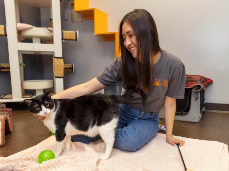 Smiling person sitting on the ground while petting a cat