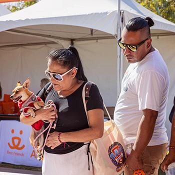 Two people and a small dog at the Los Angeles Super Adoption in front of a booth with a Best Friends logo