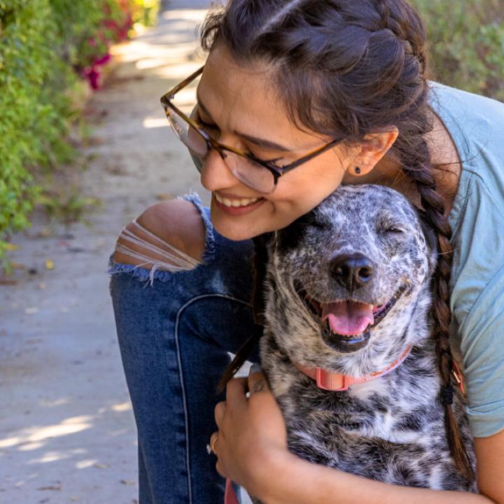 Smiling person kneeling down to hug a dog