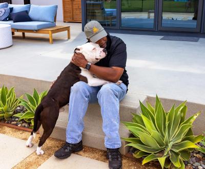 Person wearing a Best Friends hat hugging a dog while sitting on some cement steps