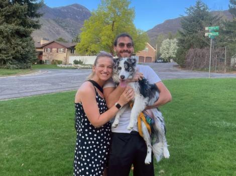 Reba Schnyder and Elliot Tolkin holding Cricket the puppy, outside on a lawn