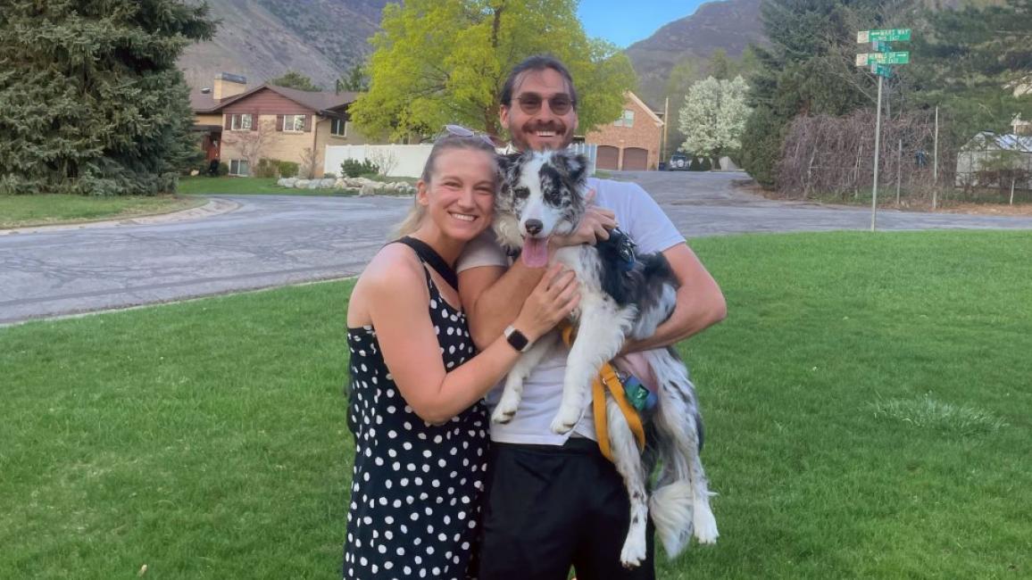 Reba Schnyder and Elliot Tolkin holding Cricket the puppy, outside on a lawn