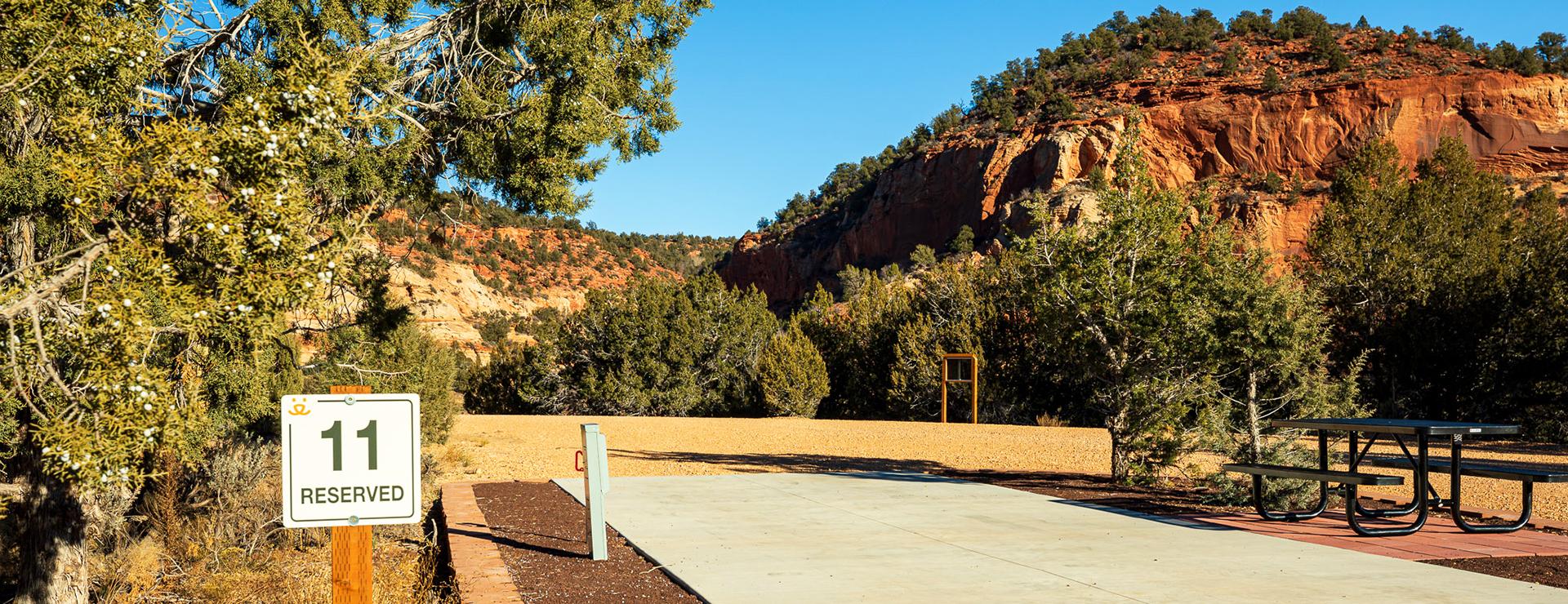 Best Friends Animal Sanctuary RV site 11 showing a sign, concrete pad, and tree and cliff behind them