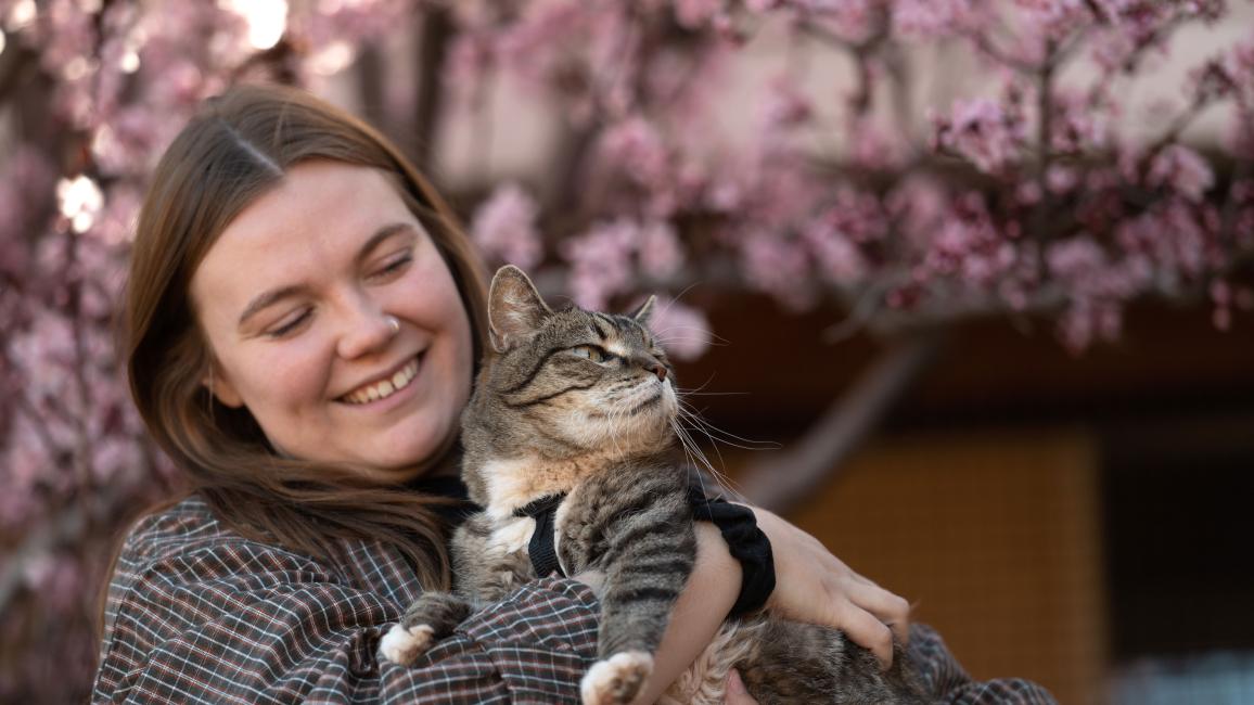 Caregiver Ashley McDaniel holding a cat in front of a flowering tree