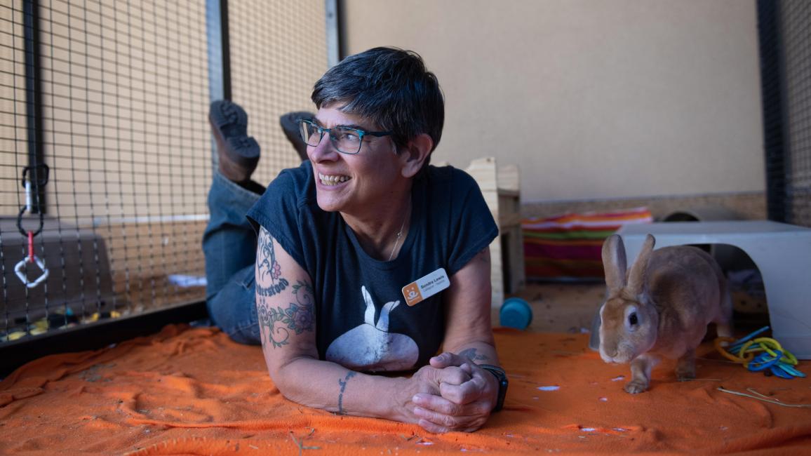 Caregiver Sondra Lewis smiling while lying next to Binky the rabbit