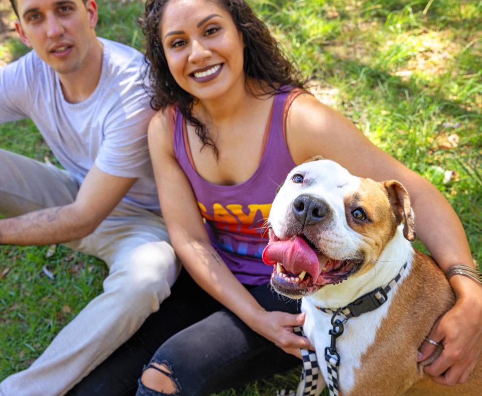 Two smiling people relaxing in the grass with their dog