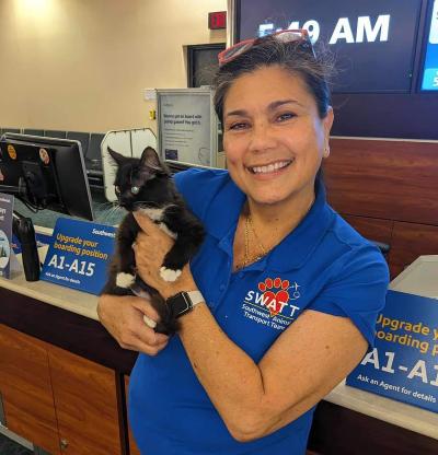 Smiling Southwest Animal Transport Team (SWATT) volunteer wearing a branded shirt holding a black and white kitten